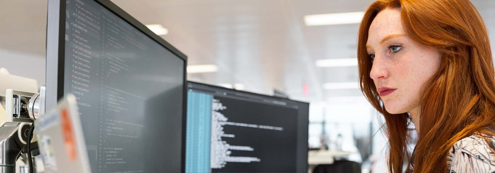 A developer at a desk with two monitors of code in a bright office