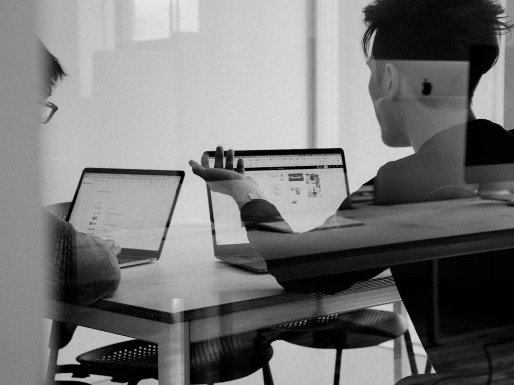 Two people in conversation over their laptops, seen through glass
